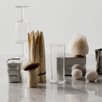 Decorative objects including a glass bottle, wooden sticks, and ceramic items on a reflective surface.