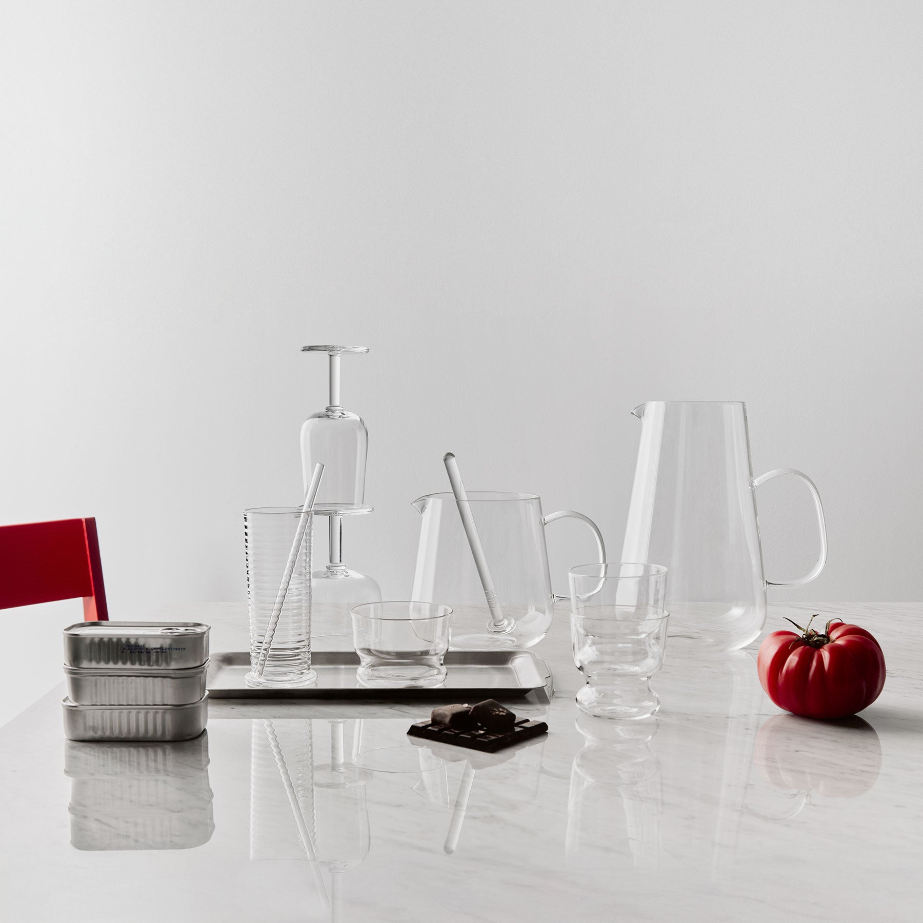Clear glassware and kitchen items on a white surface with a red tomato.