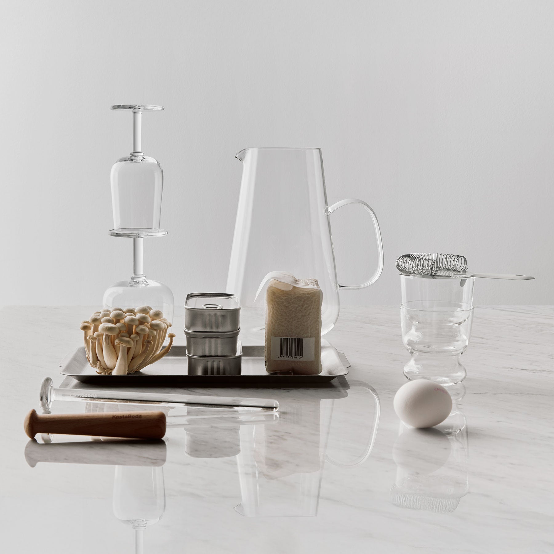 Collection of kitchen items including a pitcher, wine glass, and egg on a white surface.