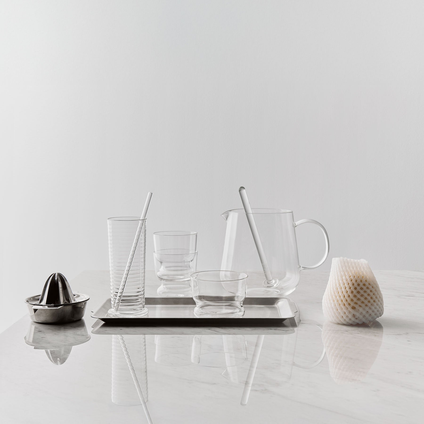 Set of glassware and kitchen tools on a marble surface with a light gray background
