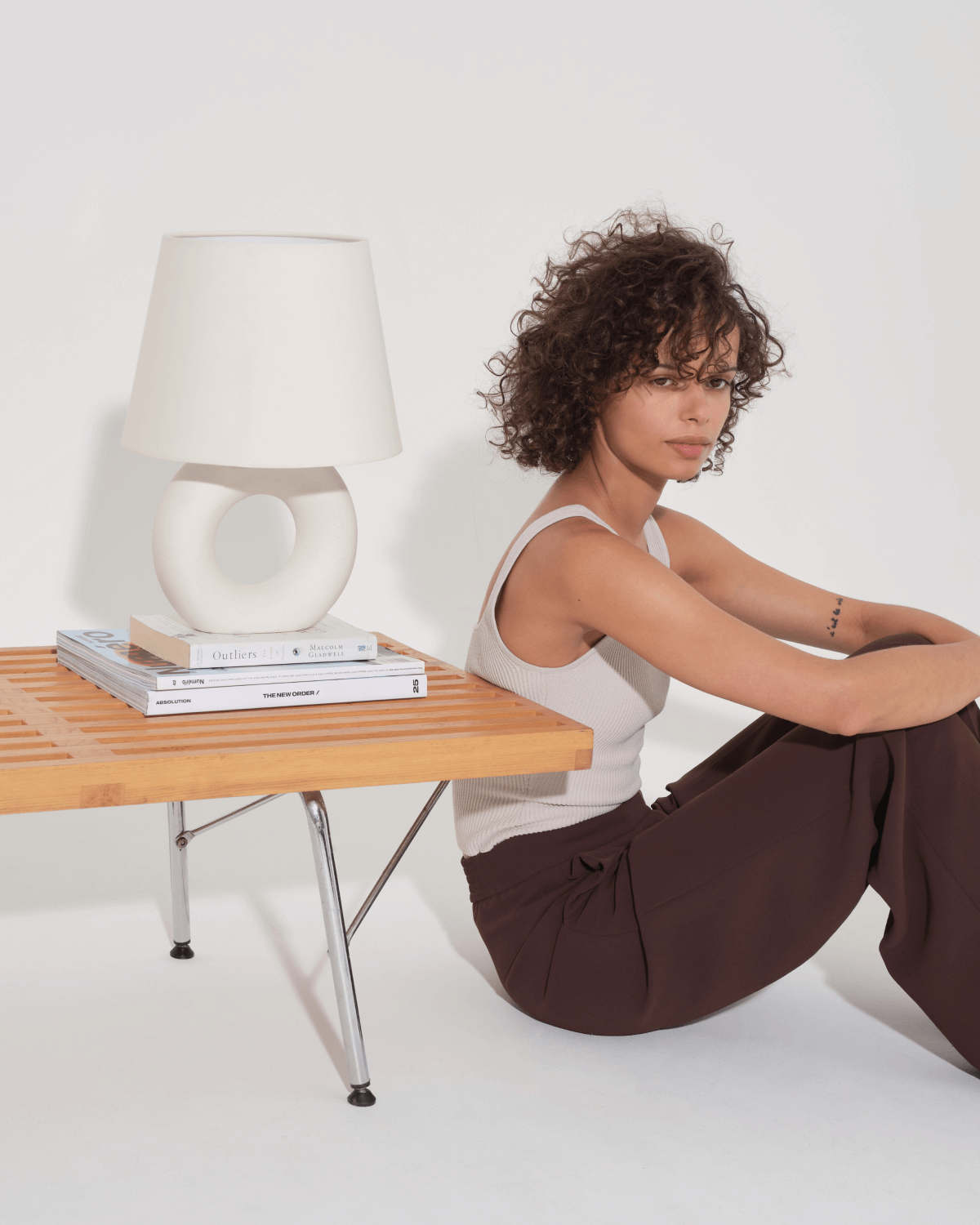 Woman sitting on the floor next to a small wooden table with a lamp and books.