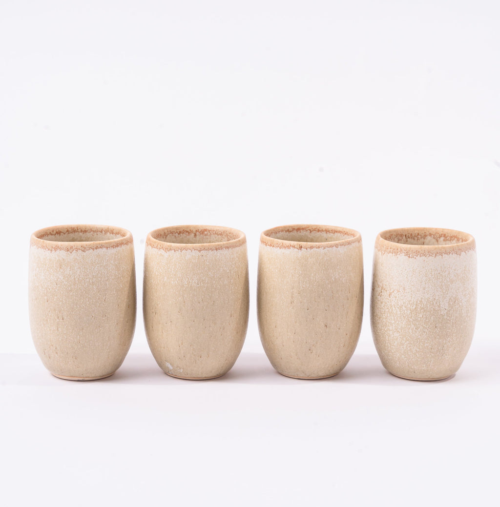 Four beige ceramic cups on a white background