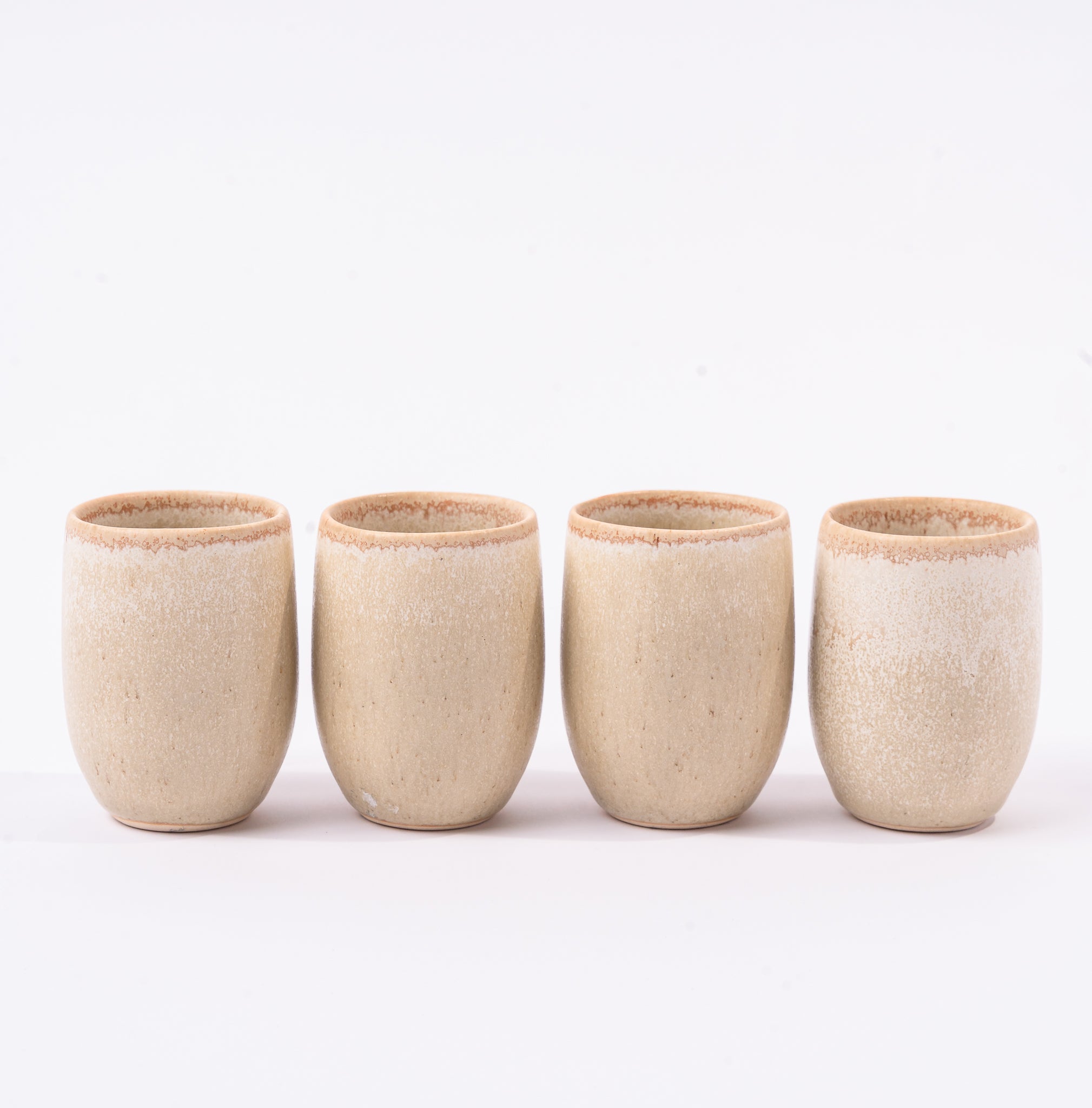 Four beige ceramic cups on a white background