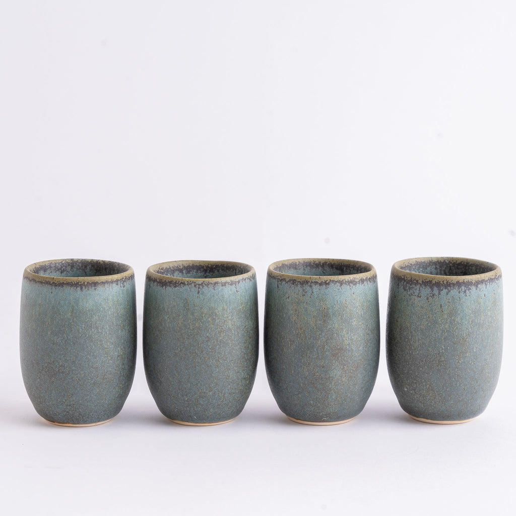 Four ceramic cups with a blue-green glaze on a white background