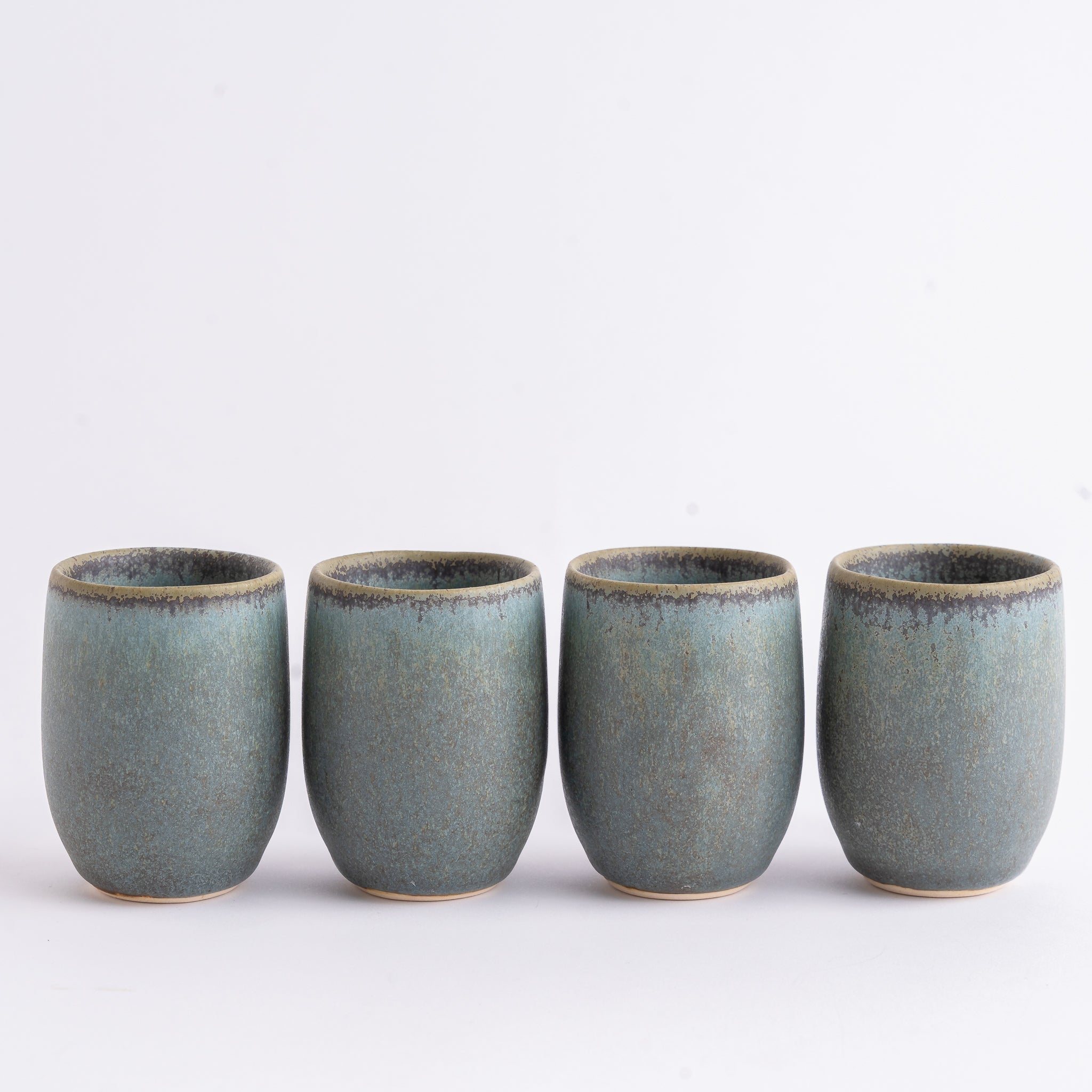 Four ceramic cups with a blue-green glaze on a white background