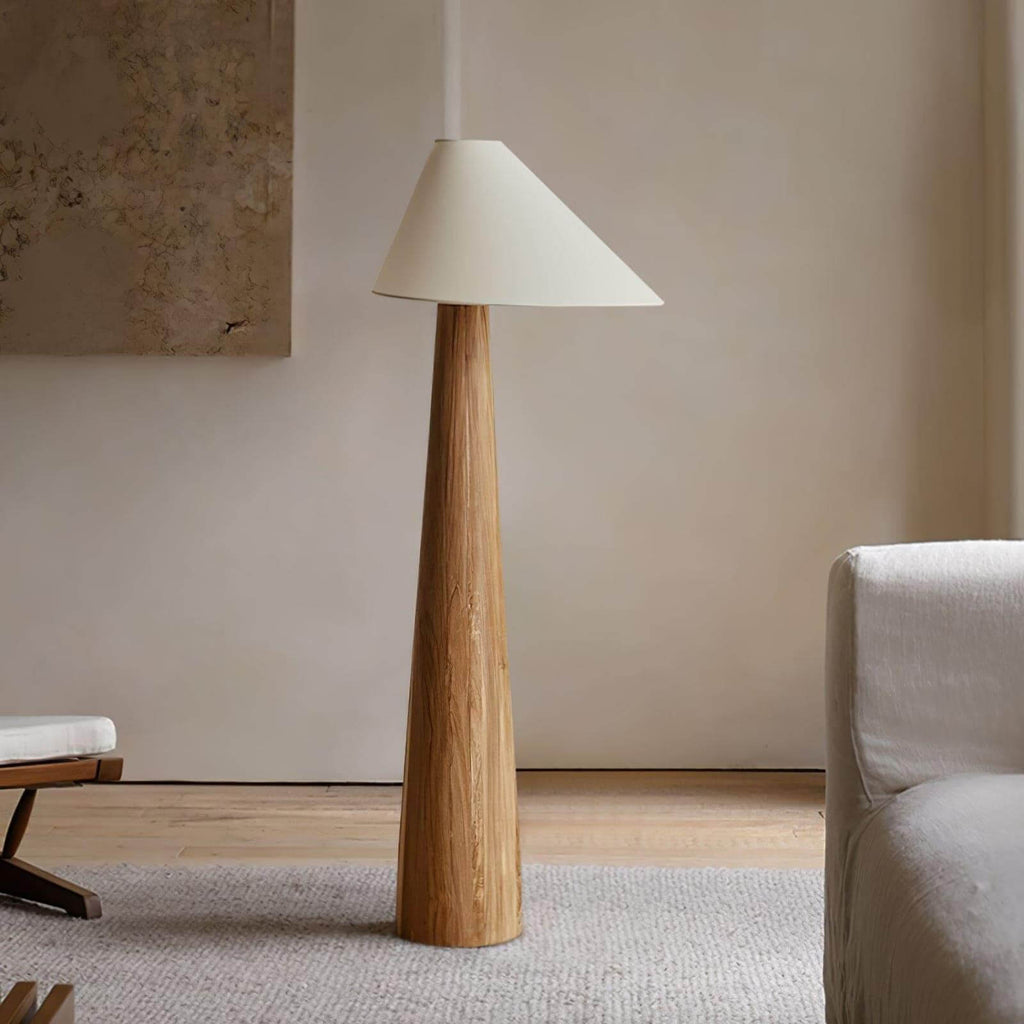 Wooden floor lamp with a white shade in a room with a beige wall and a sofa.