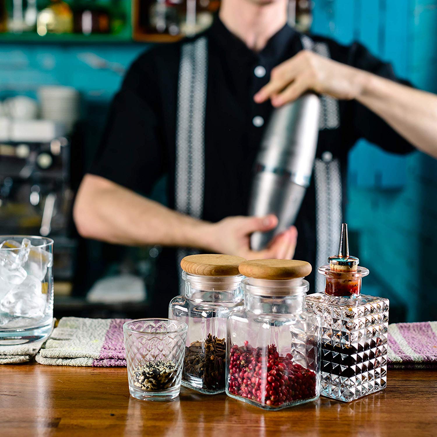 Barista preparing a drink with jars of ingredients on a bar counter.