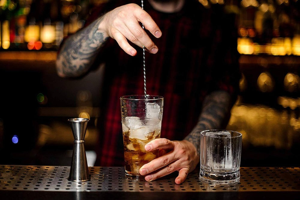 Bartender preparing a cocktail with ice and a strainer in a bar setting