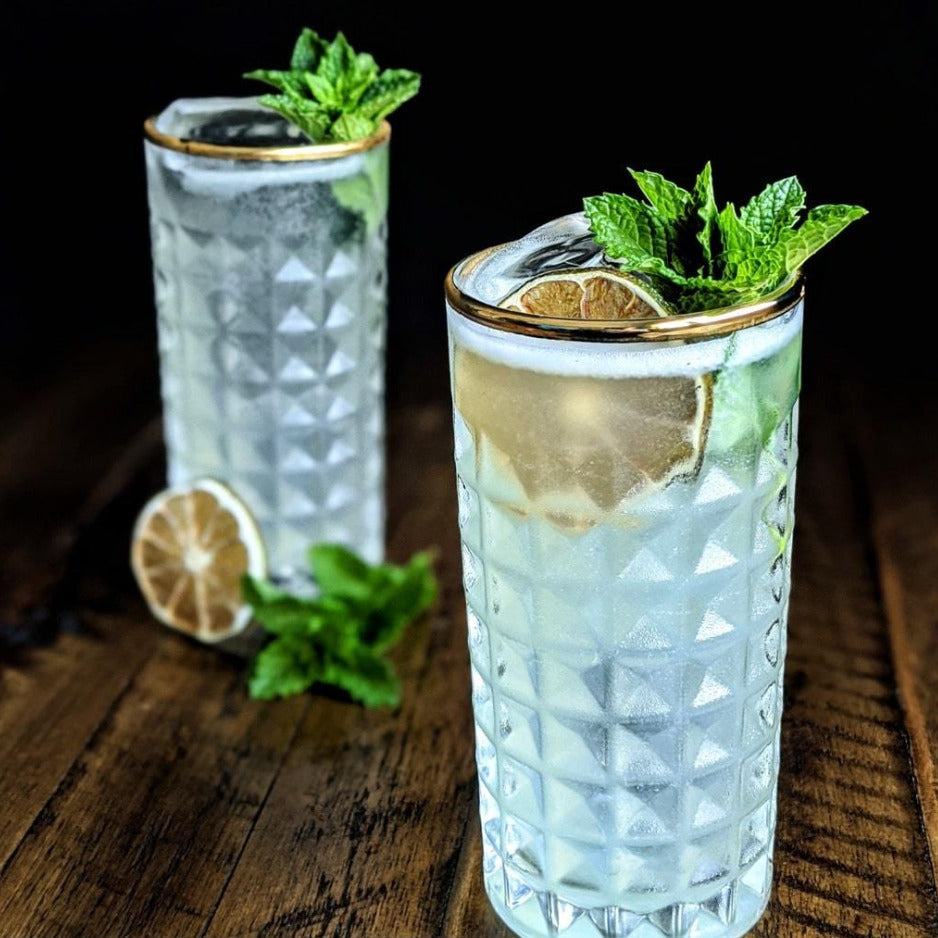 Two diamond-patterned glasses filled with a clear drink, garnished with lime and mint leaves on a wooden surface.