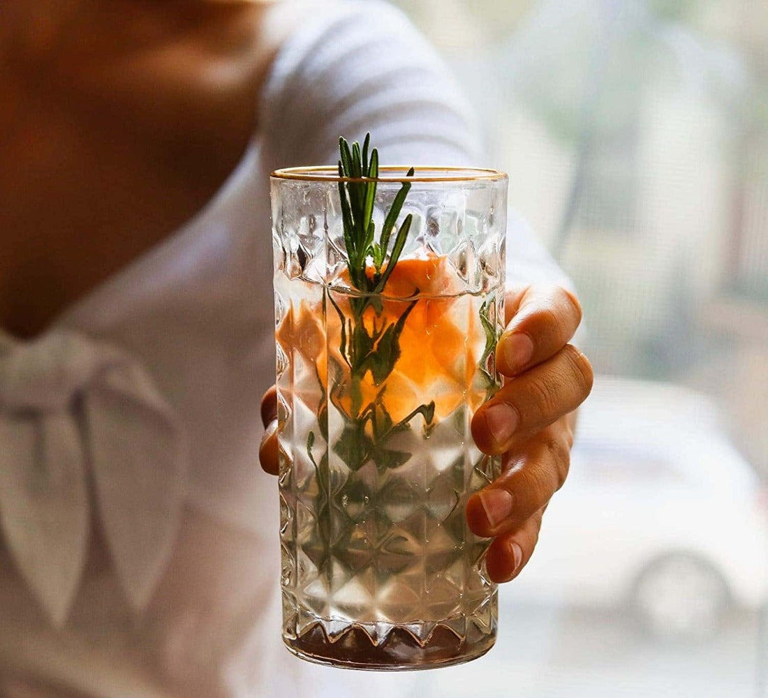 Hand holding a glass with a cocktail garnished with orange slices and rosemary.