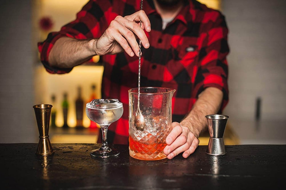 Person making a cocktail at a bar with various tools and ingredients.