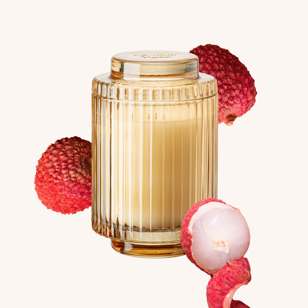 Candle in a ribbed glass container with lychee fruits on a white background