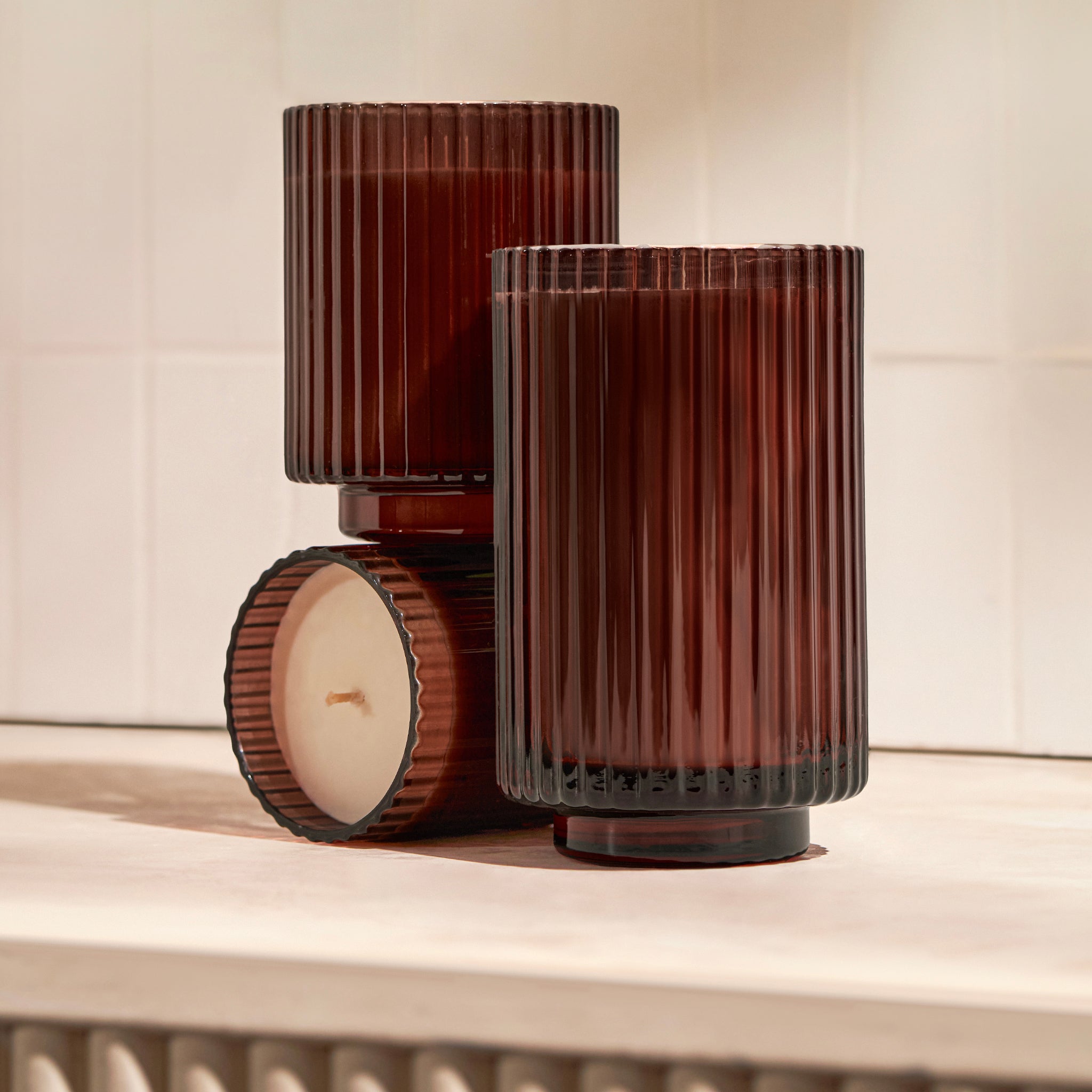 Two brown ribbed glass candle holders with candles on a light wooden surface.