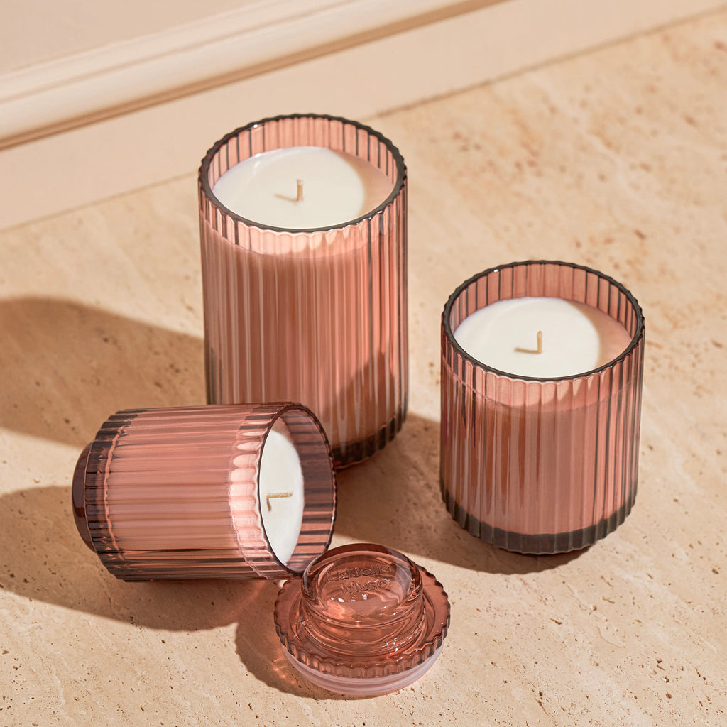 Three ribbed glass candle holders with candles on a wooden surface