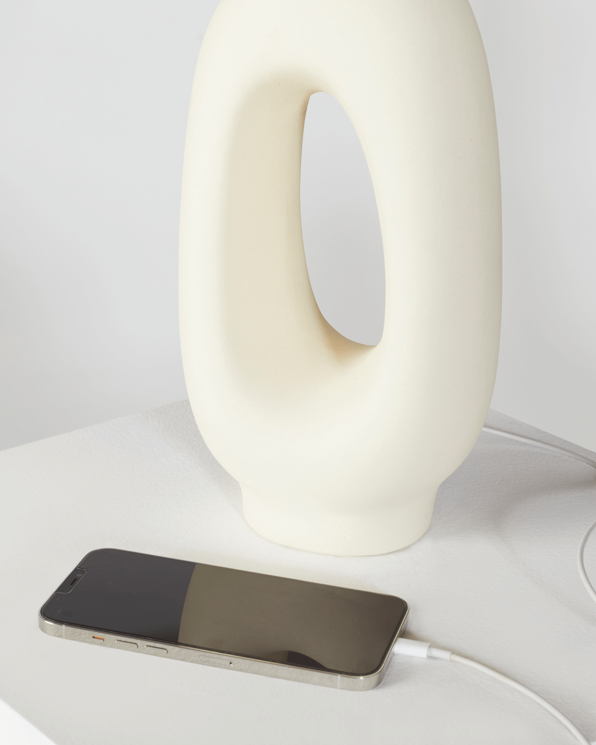 Phone charging on a white surface with a modern white lamp in the background