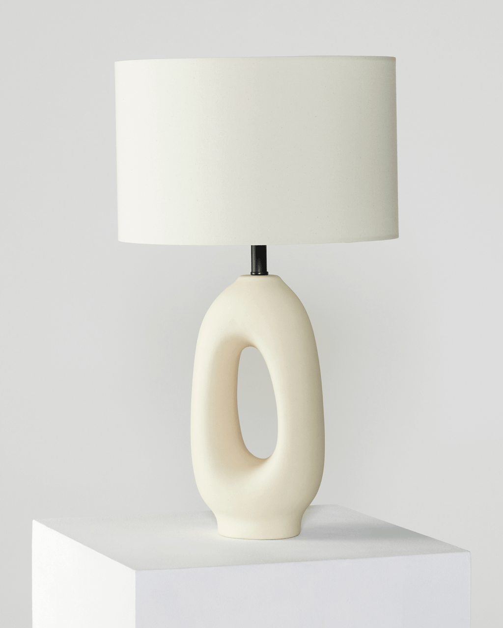 Table lamp with a white ceramic base and beige lampshade on a light gray background