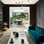Modern living room with teal sofa, coffee table, and open door to patio.