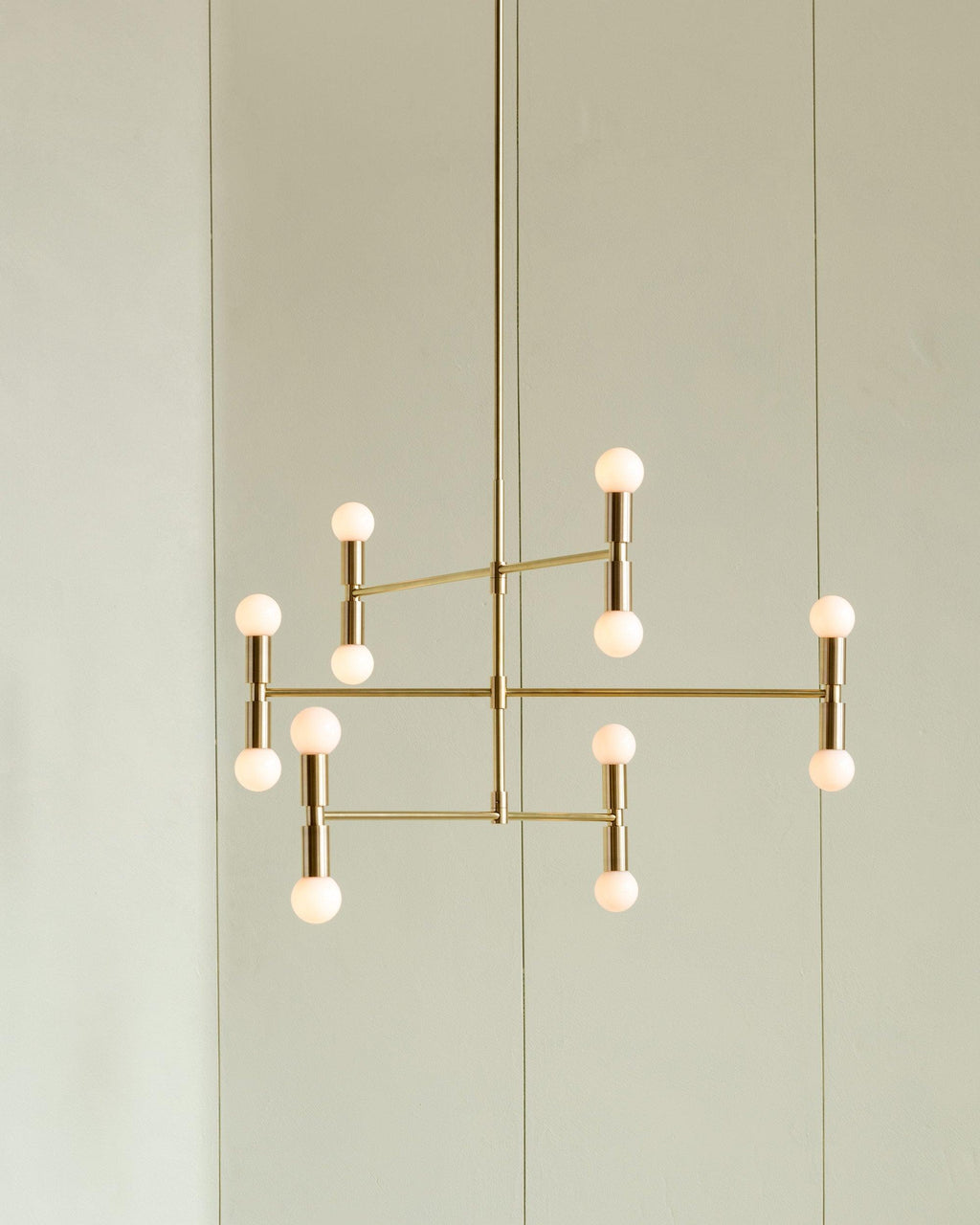 Modern gold chandelier with multiple light bulbs against a light green wall.