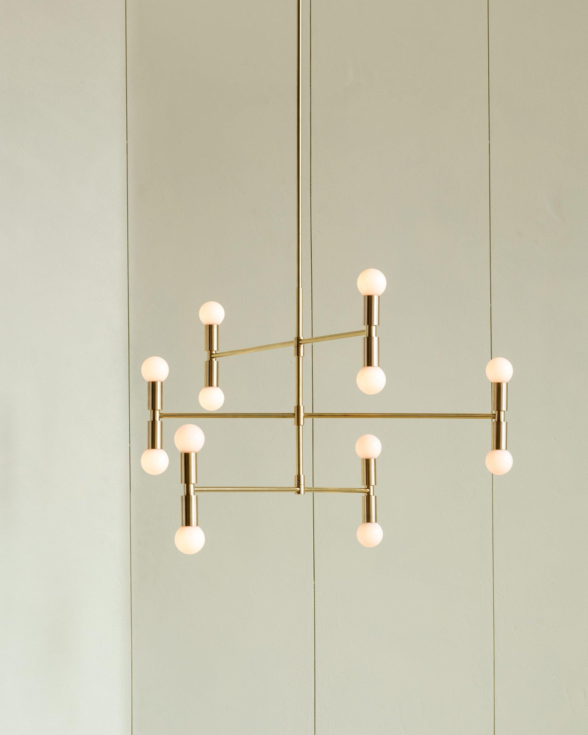 Modern gold chandelier with multiple light bulbs against a light green wall.