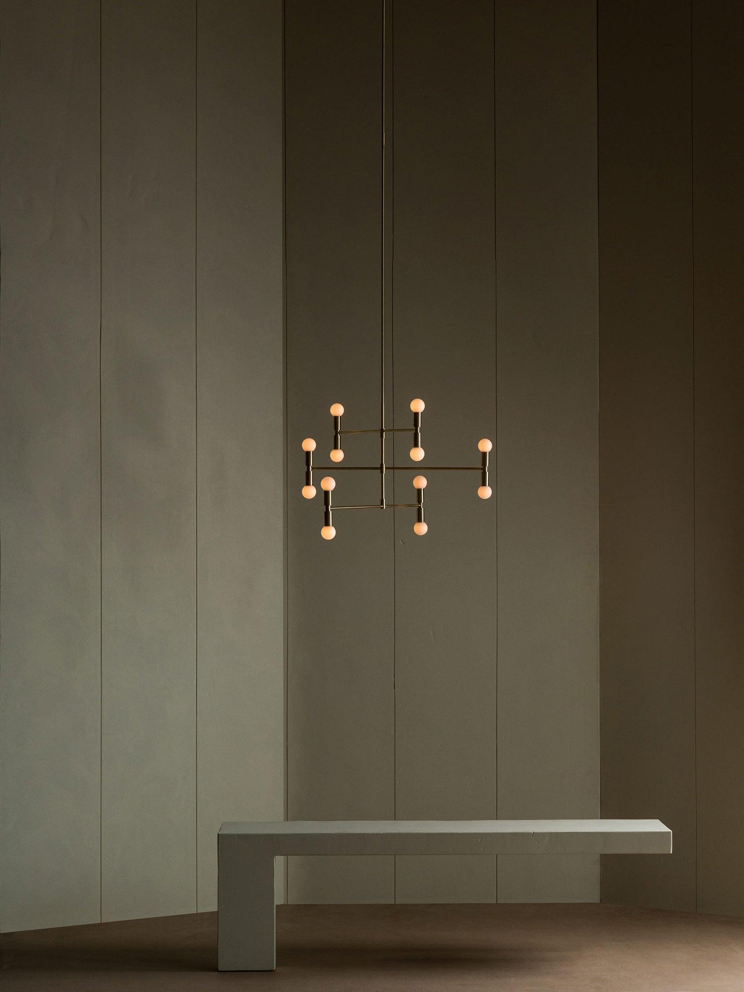 Modern chandelier hanging above a concrete bench against a dark wall.