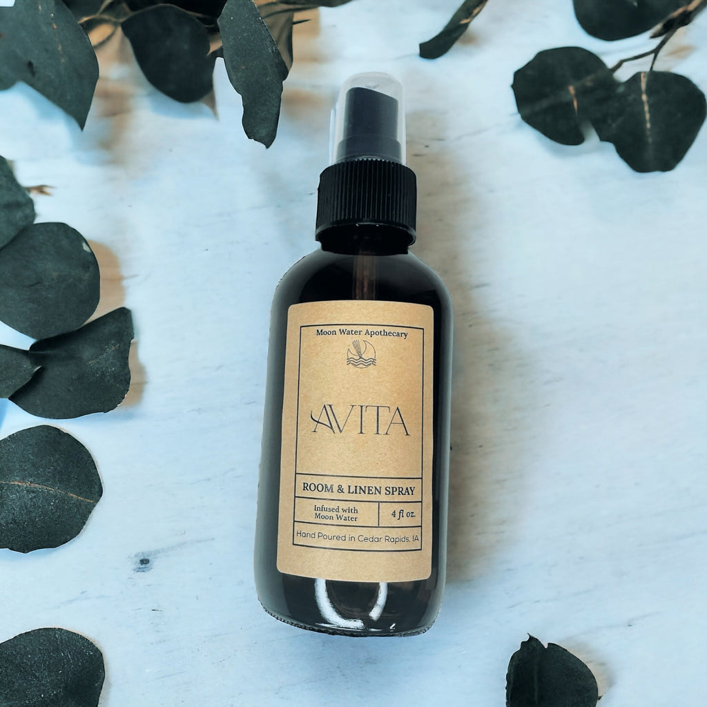 Room & Linen Spray bottle with Savita label on a light wooden surface with dark green leaves.