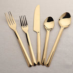 Set of gold cutlery including forks, knives, and spoons on a light gray background