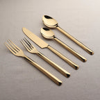 Set of gold cutlery including knife, fork, and spoons on a gray background