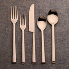 Set of rose gold cutlery including fork, knife, and spoons on a textured brown surface.