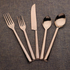 Set of rose gold cutlery including forks, a knife, and two spoons on a textured brown surface.