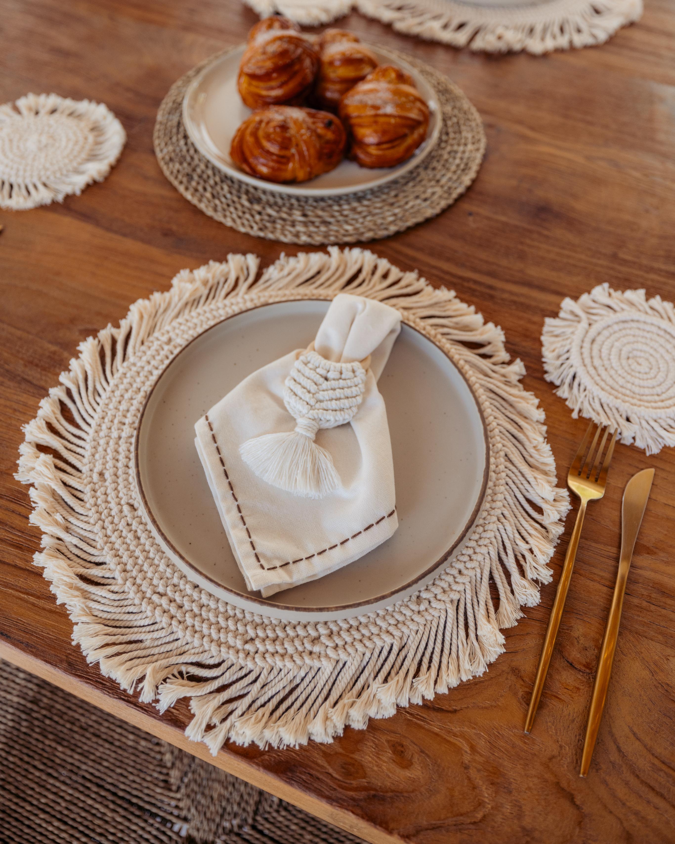Table setting with macrame placemats, gold cutlery, and a plate of pastries.