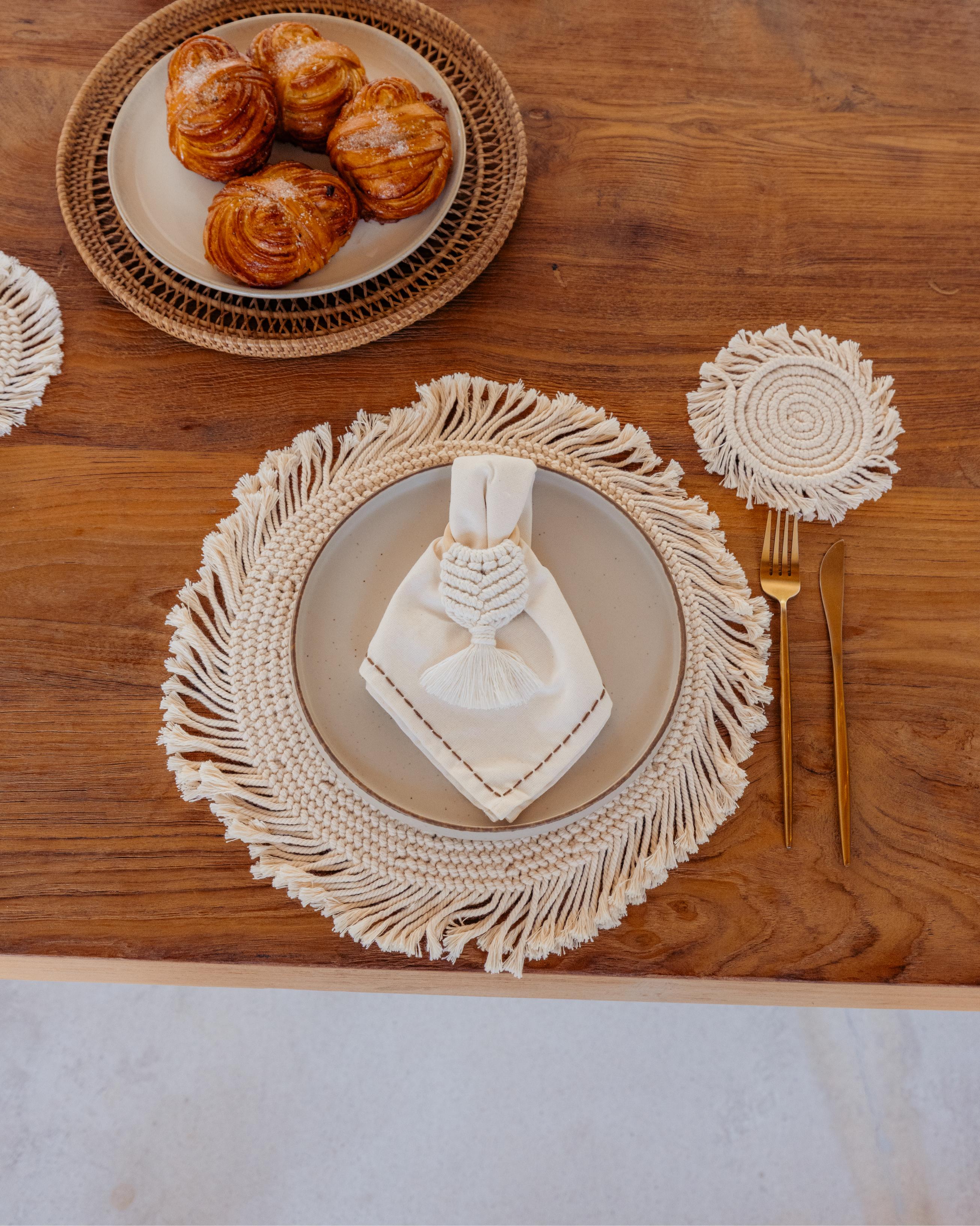 Table setting with macrame placemat, gold fork, and pastries on a wooden table.