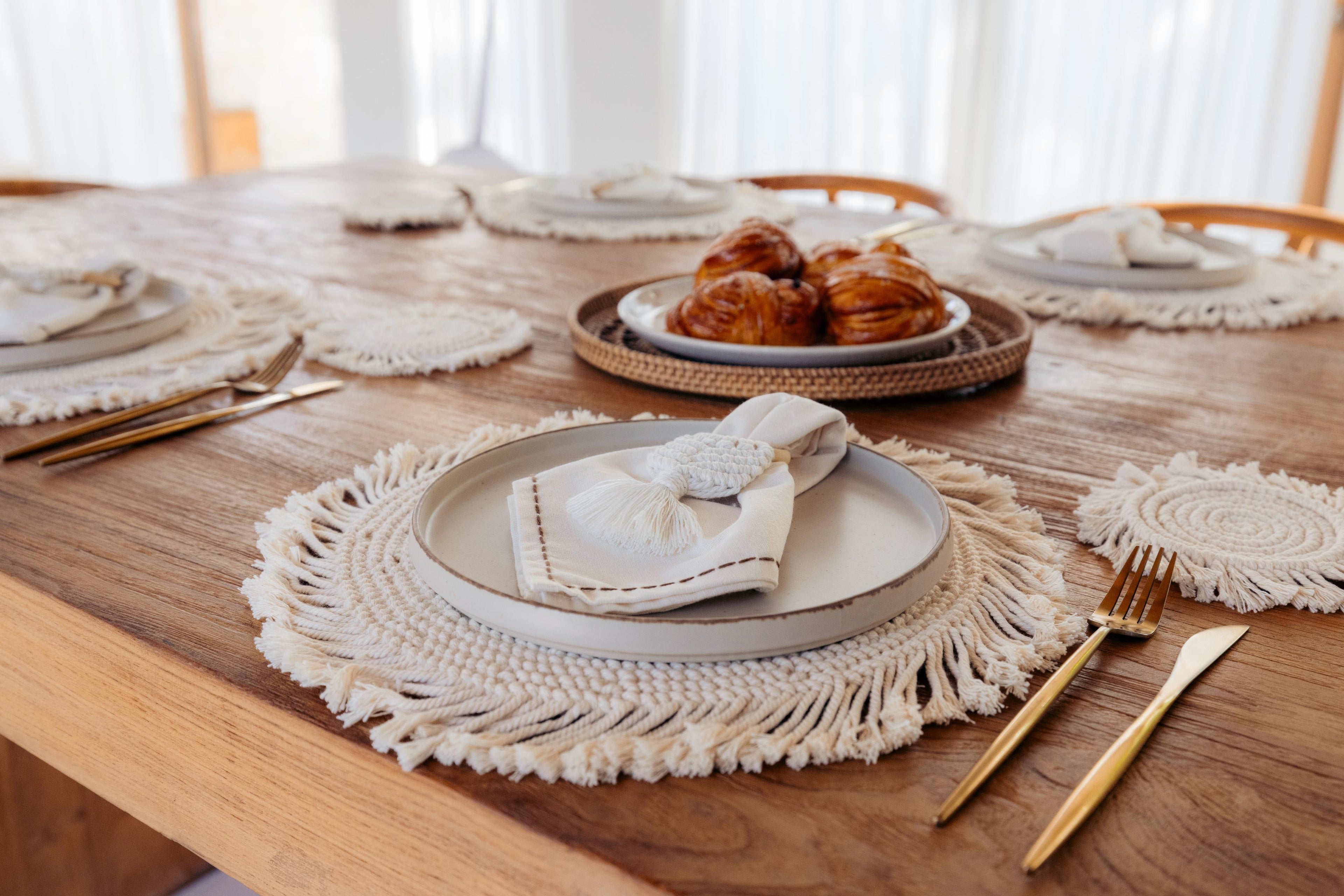 Dining table set with plates, napkins, and gold cutlery on a wooden table.