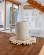 Speckled ceramic mug on a wooden surface with a textured coaster