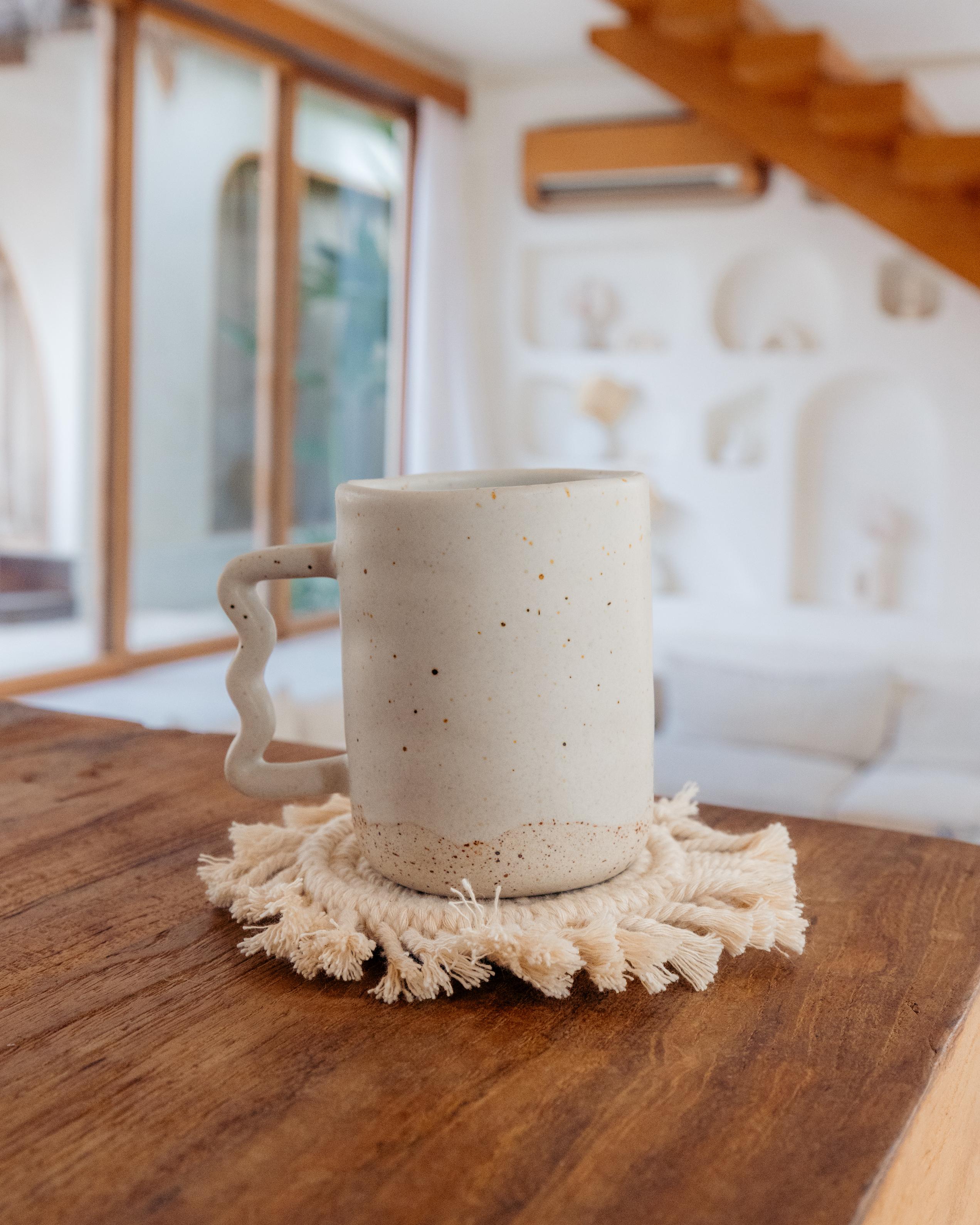 Speckled ceramic mug on a wooden surface with a textured coaster