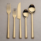 Set of gold cutlery including fork, knife, and spoons on a gray background