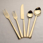 Set of gold cutlery including forks, knife, and spoons on a gray background