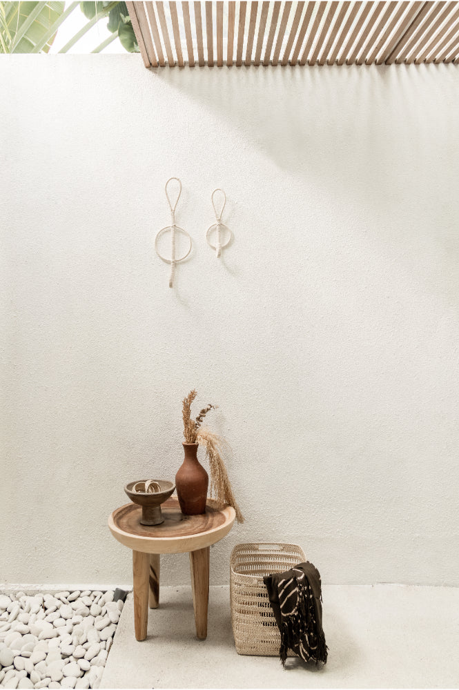 Small wooden table with decorative items against a white wall and woven basket.