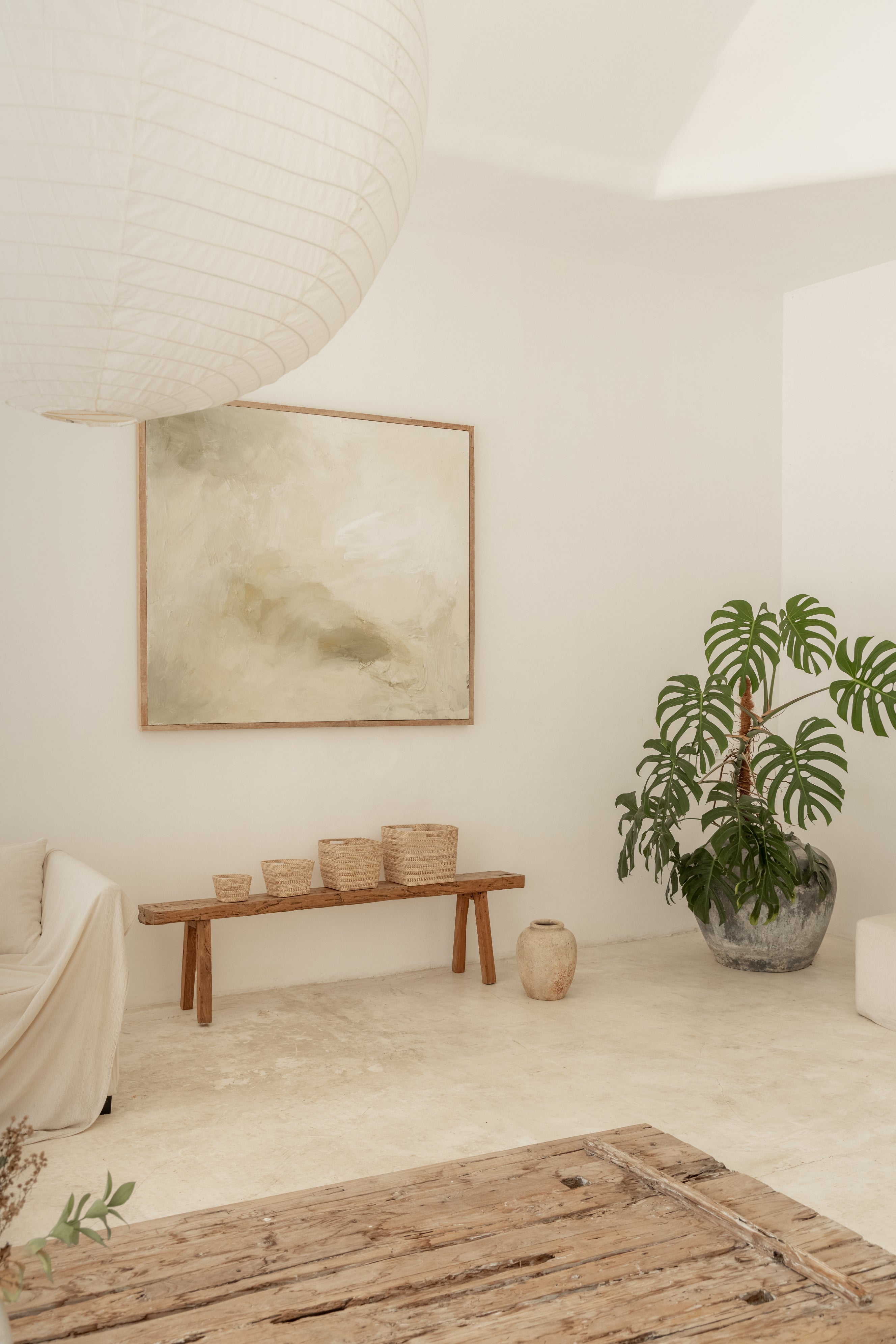 Modern interior with a wooden bench with baskets on top, potted plant, and abstract painting on a white wall.