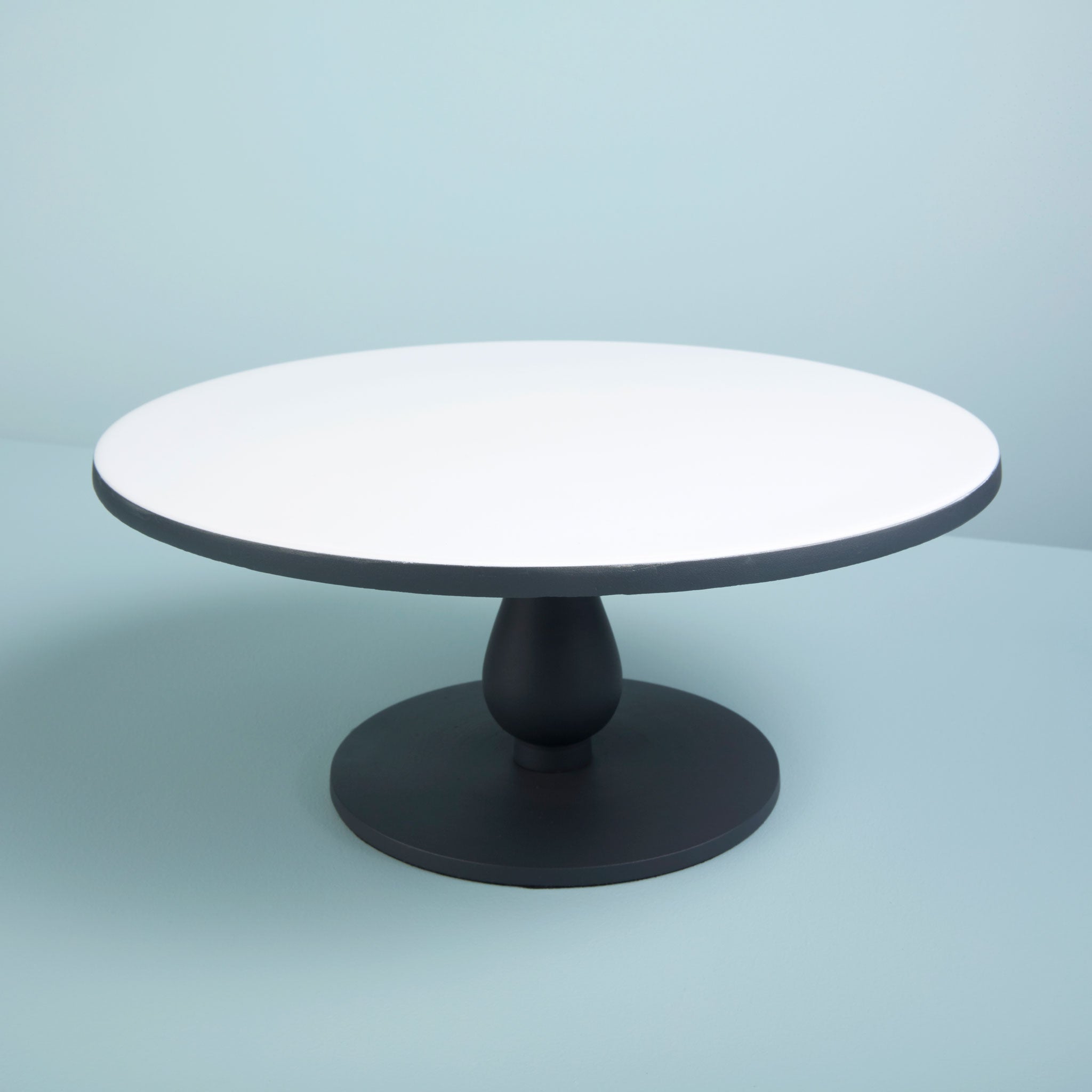 Round cake stand with white top and black base on a light blue background