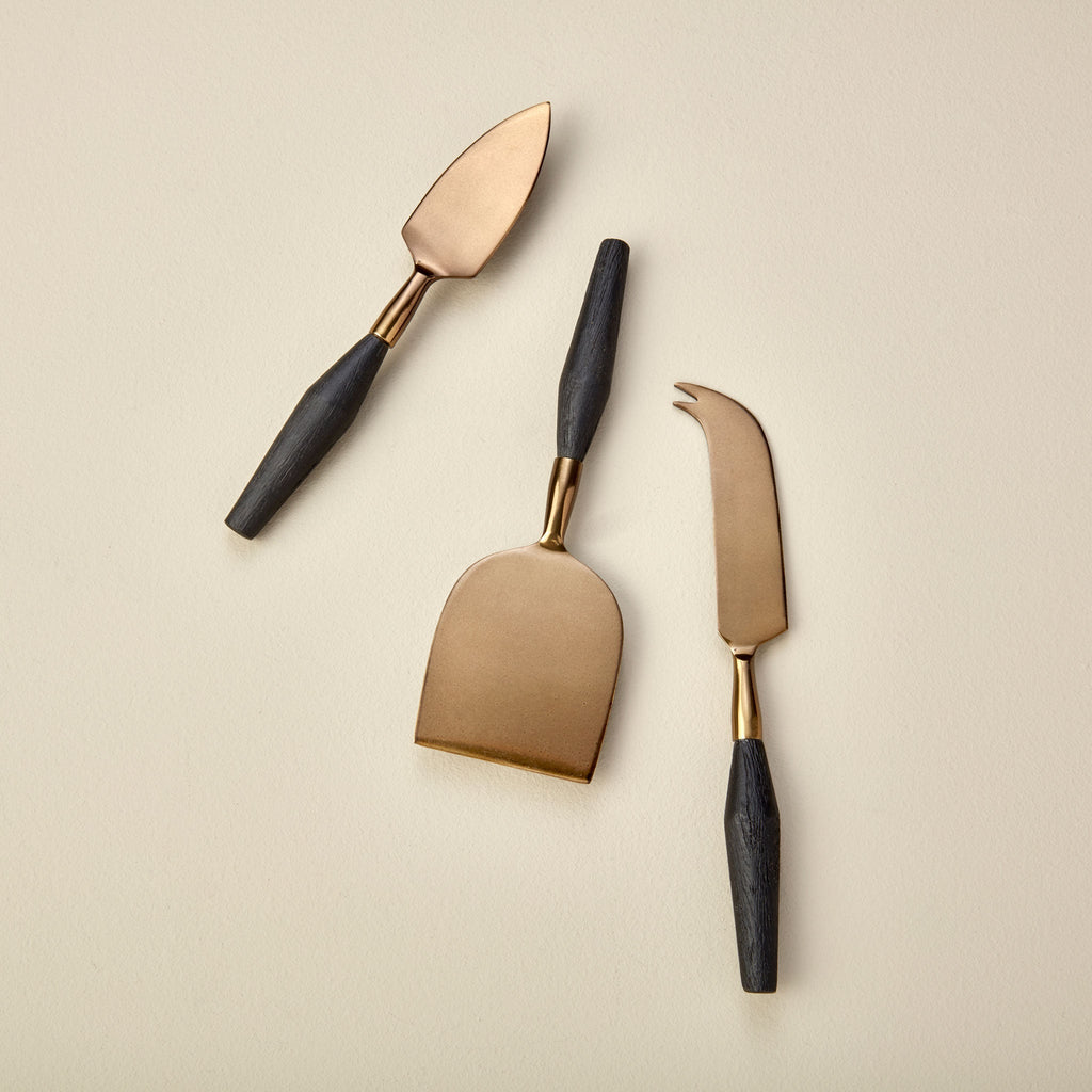 Three cheese knives with black handles on a beige background