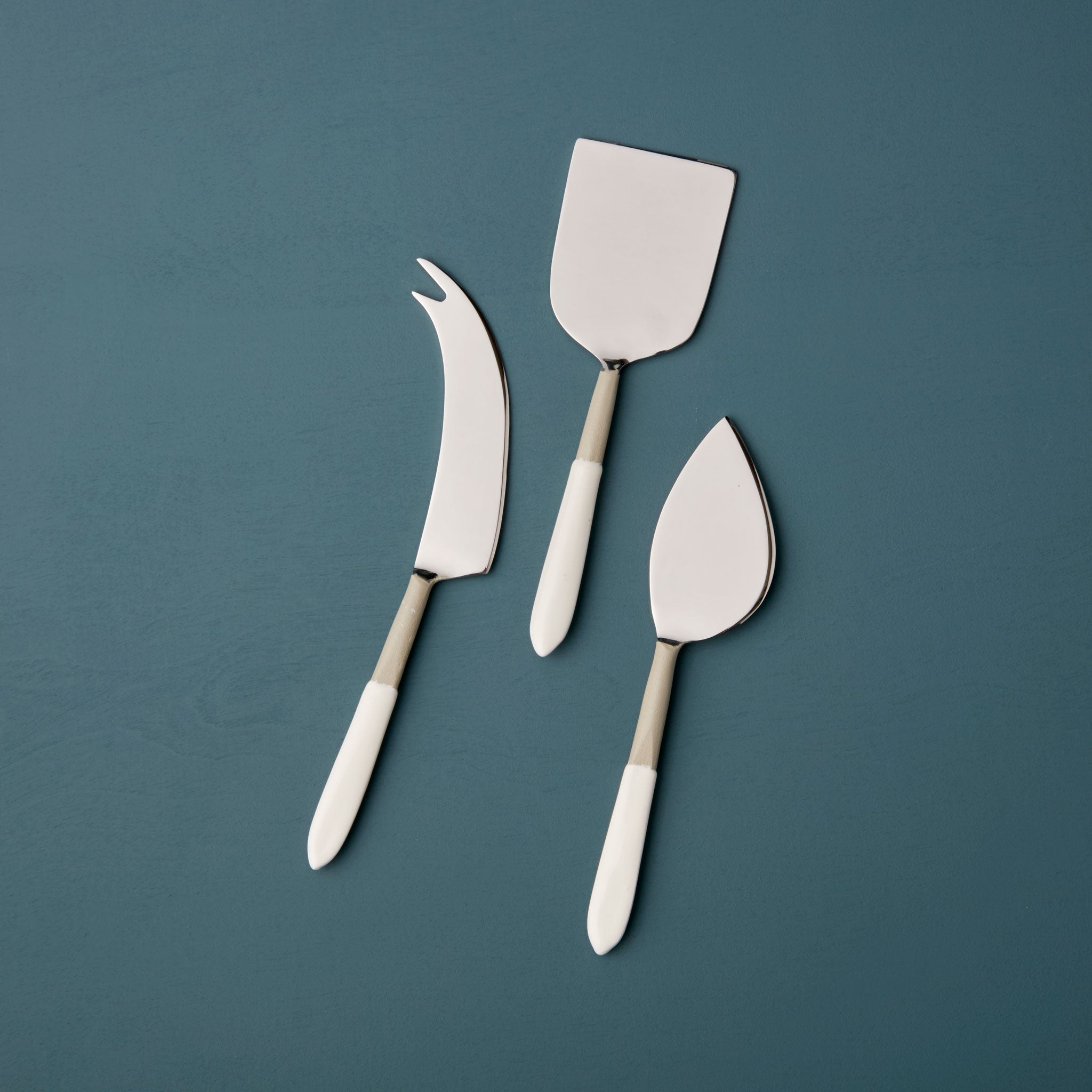 Set of three cheese tools on a teal background