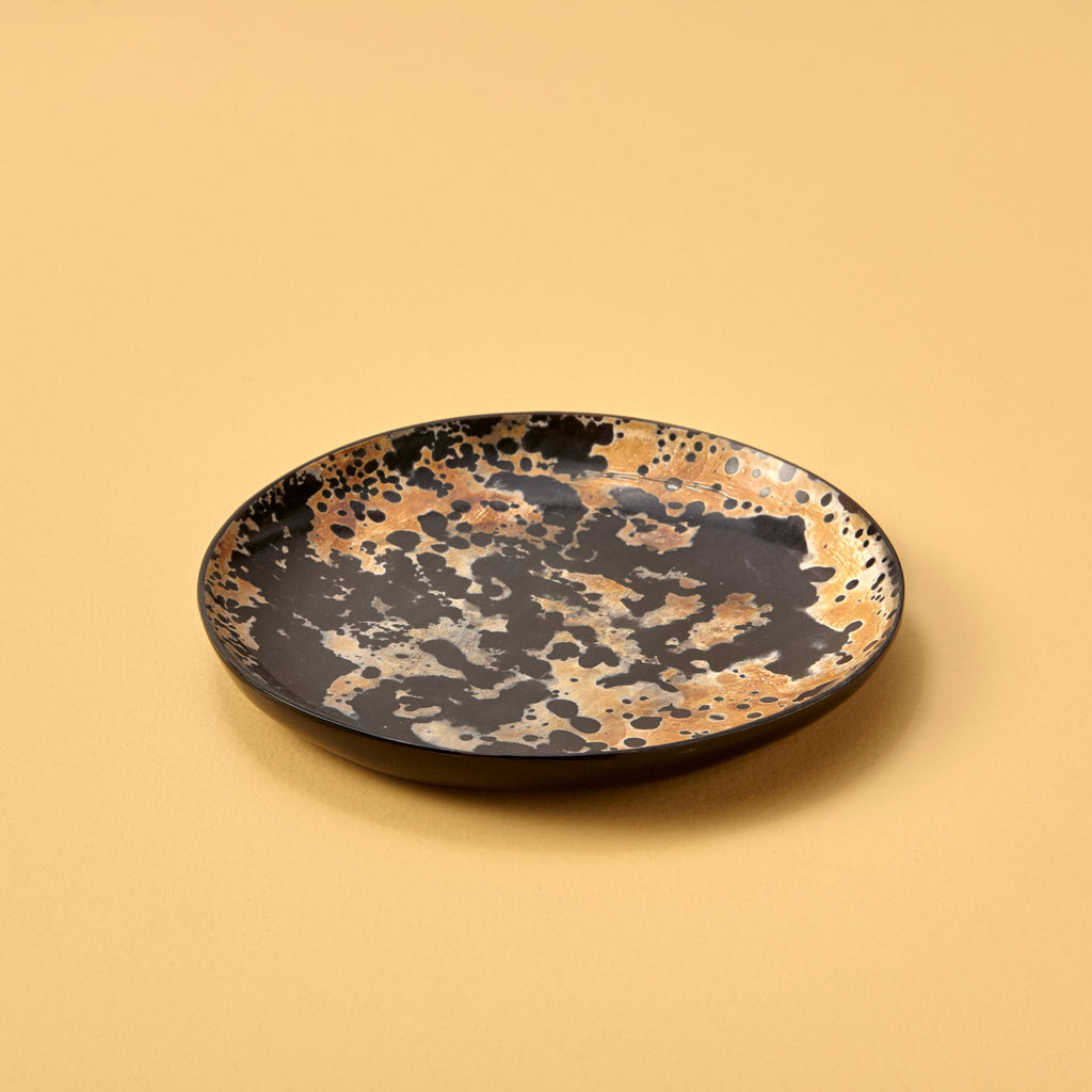 Ceramic plate with black and gold speckled pattern on a beige background