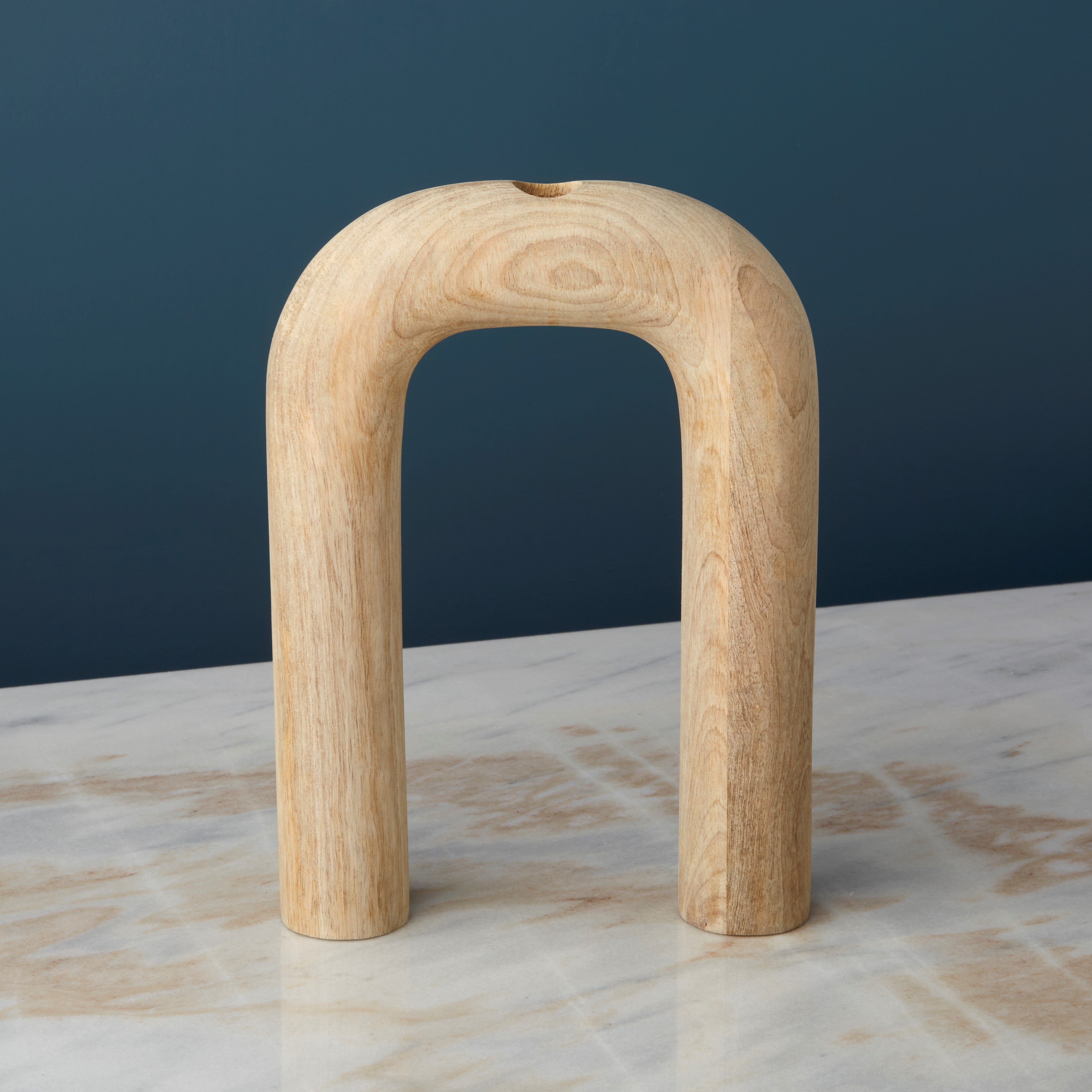 Wooden arch sculpture vase on a marble surface with a dark blue background
