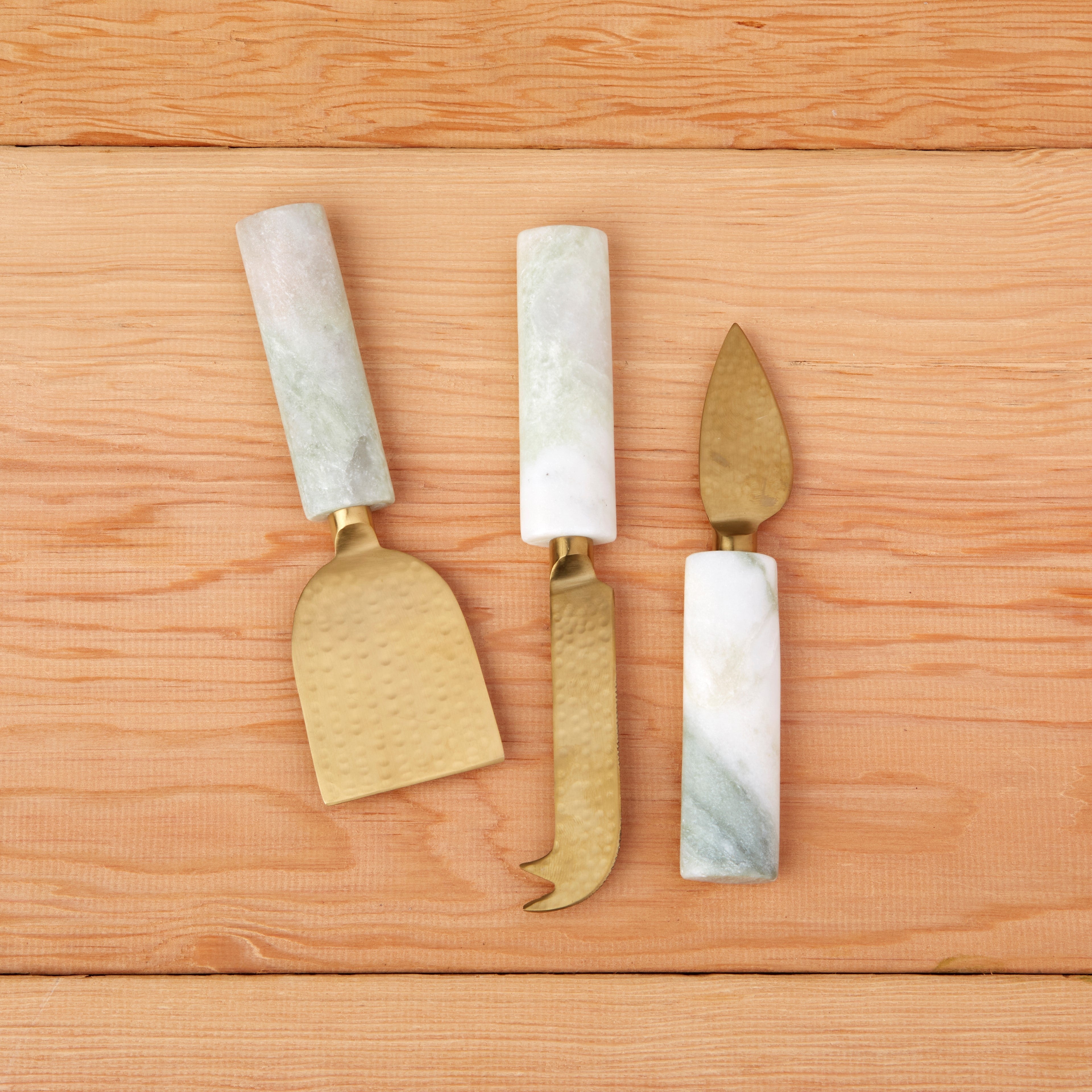 Three cheese knives with marble handles on a wooden surface