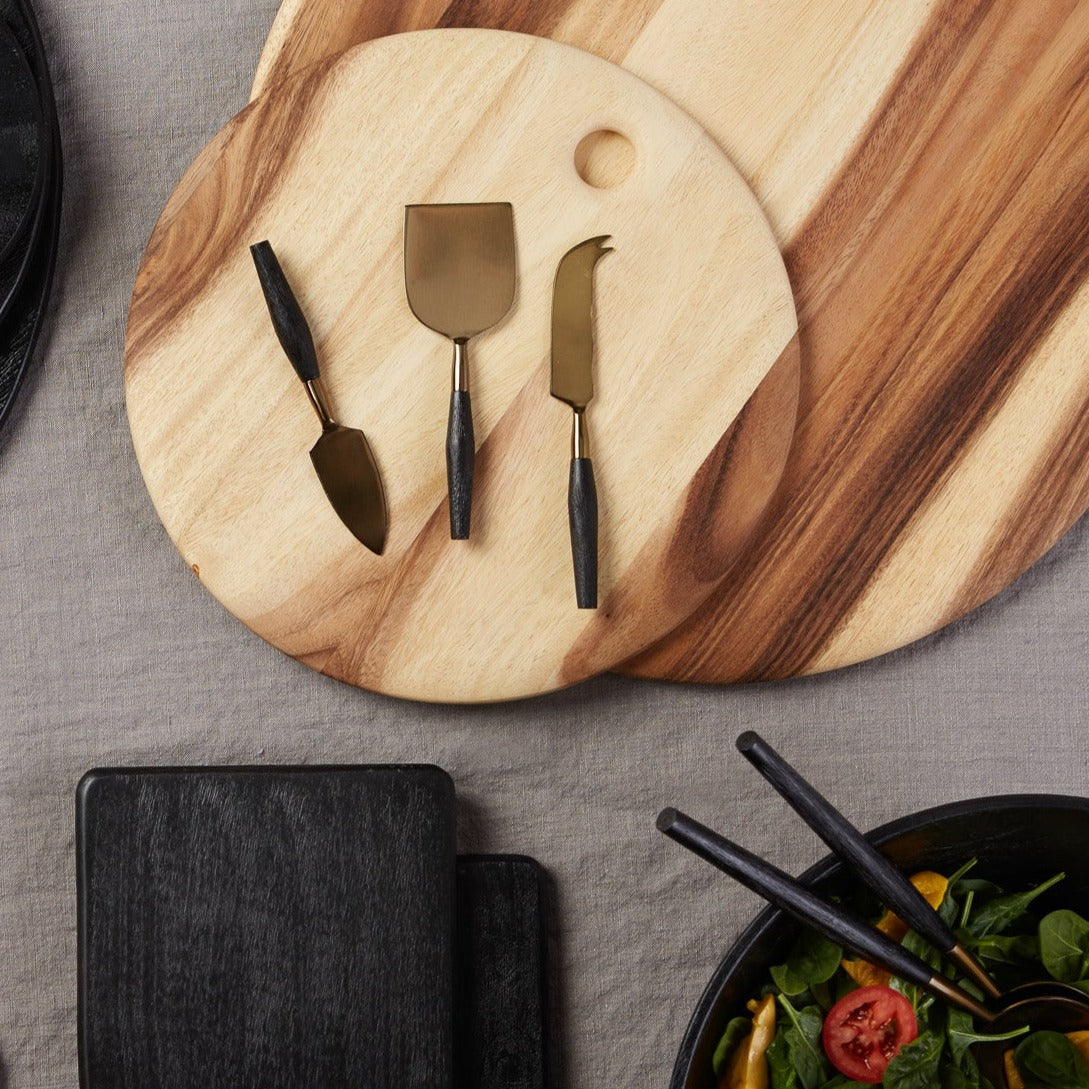 Wooden cutting board with cheese knives on a gray surface