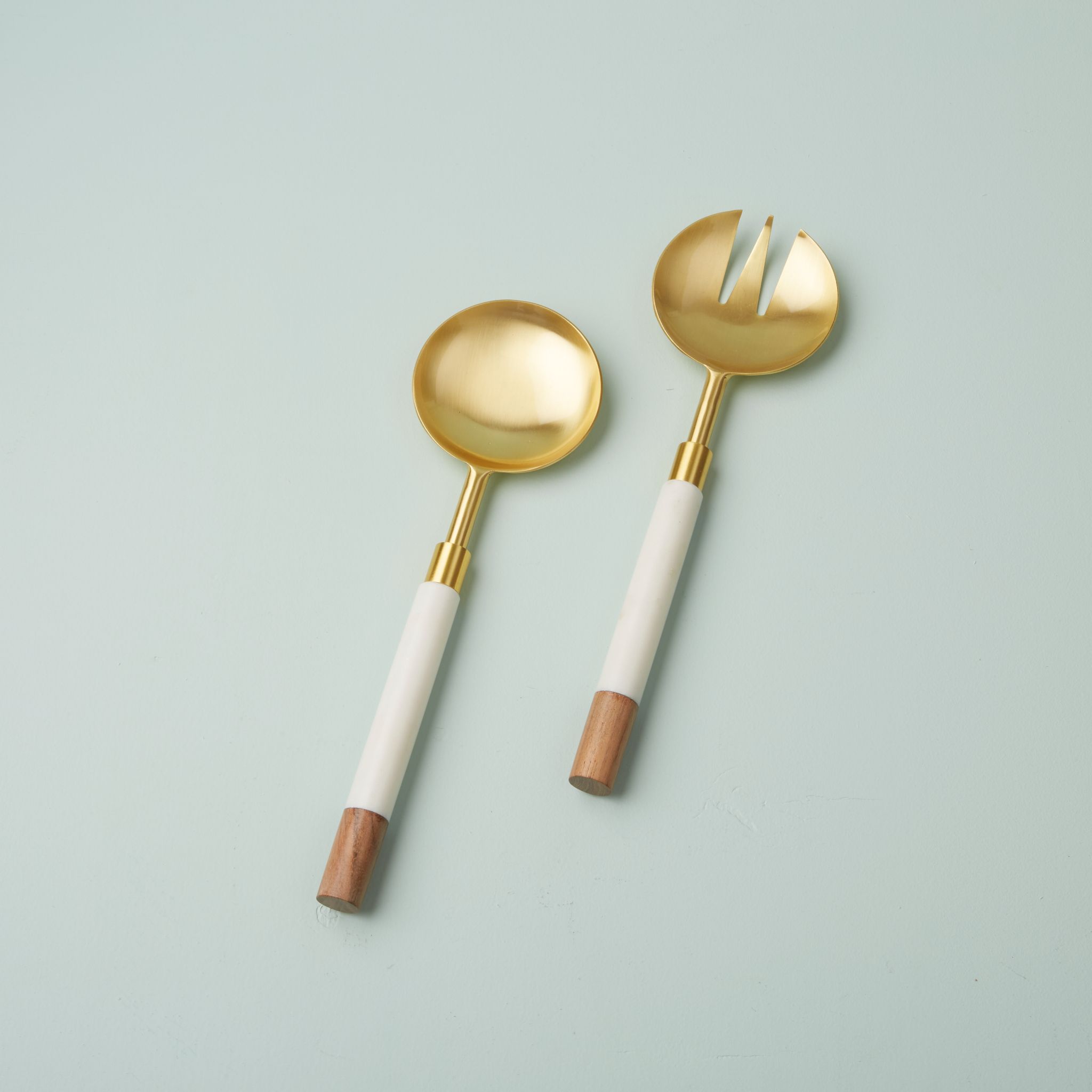Gold-handled spoon and fork with white handles on a light blue background