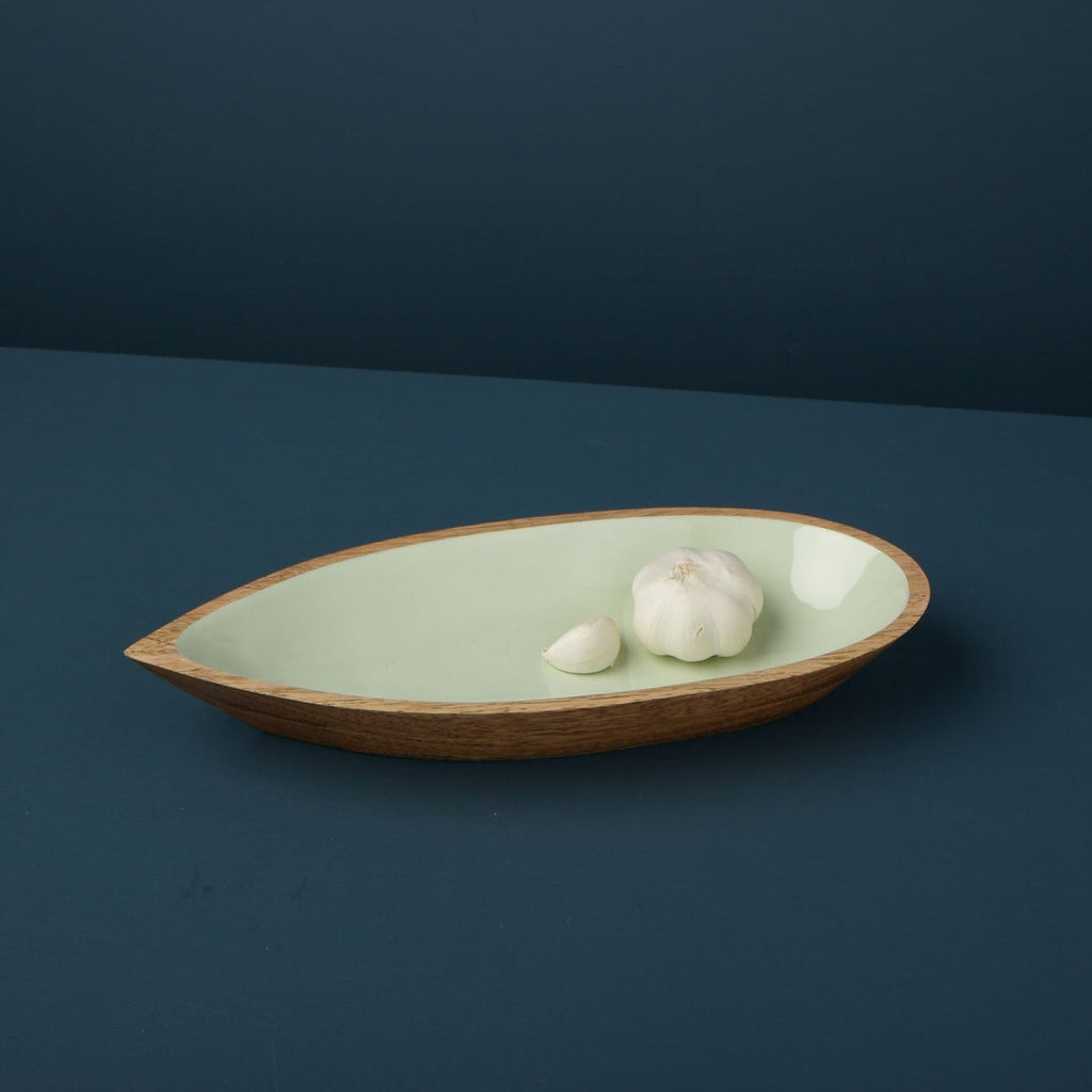 Wooden bowl with a green interior containing garlic cloves on a dark blue background