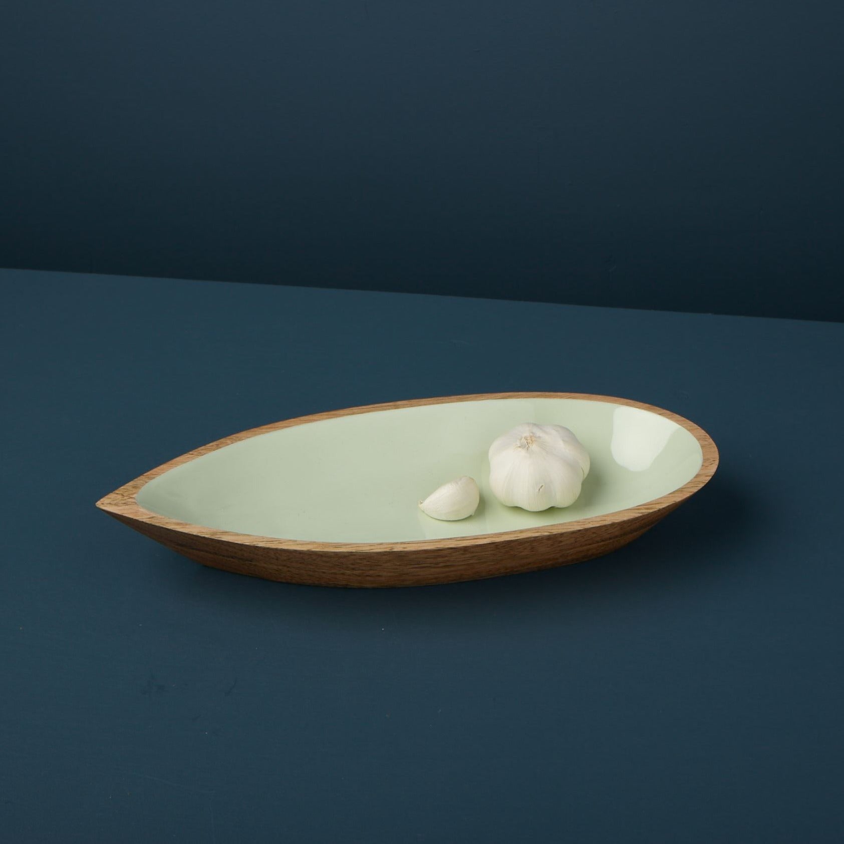 Wooden bowl with a green interior containing garlic cloves on a dark blue background
