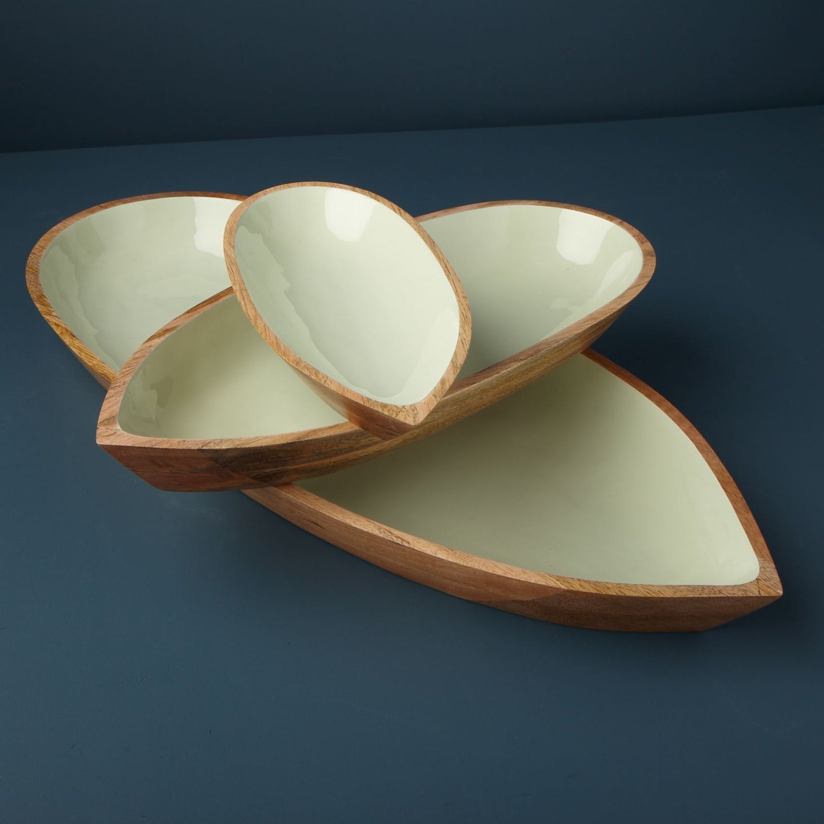 Three wooden bowls with green interiors on a dark blue background