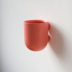 Coral-colored cup hanging on a white wall